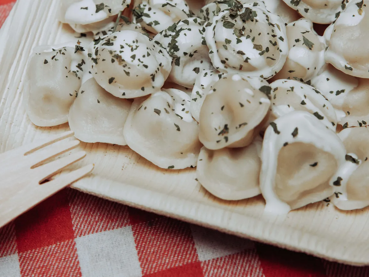 Des pelmeni parsemés d'herbes, servis dans une barquette en bois sur une nappe vichy.