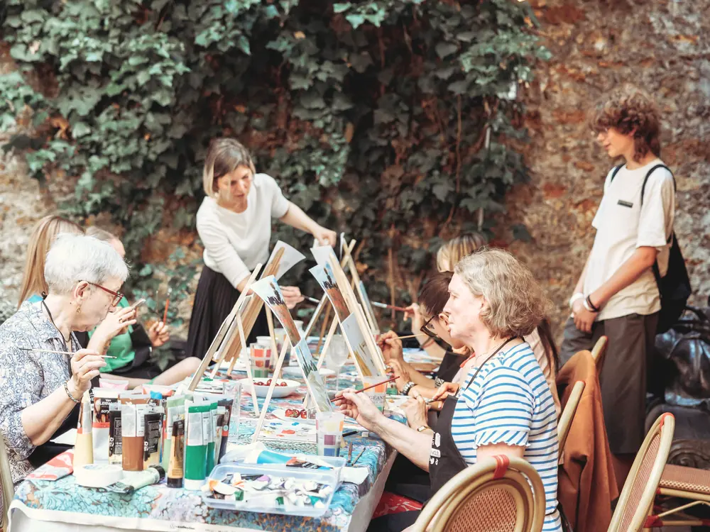 Un atelier créatif sur la terrasse : un groupe réuni autour d'une grande table, sous les guirlandes et le mur végétal.