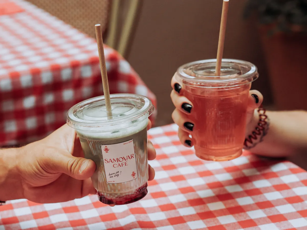 Deux boissons signature glacées du Samovar Café, tenues au-dessus d'une table vichy.