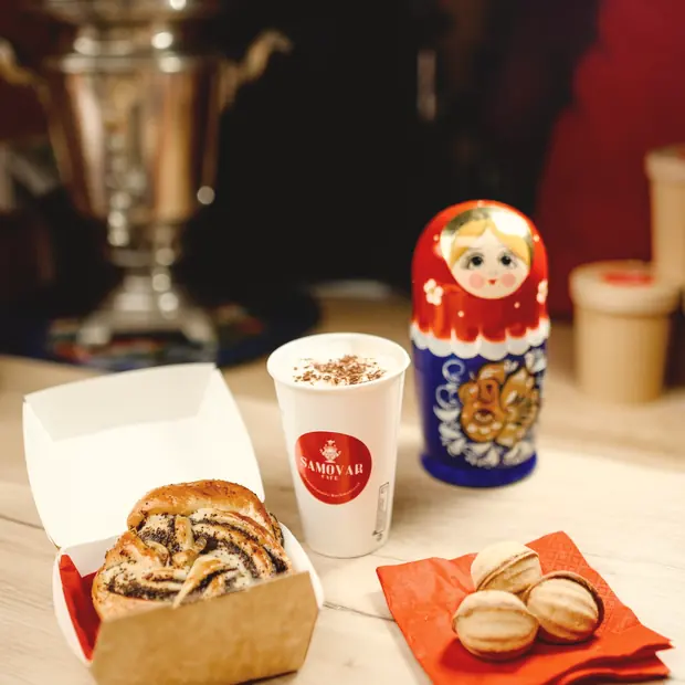 Un samovar en cuivre, une matriochka, un gobelet du Samovar Café et une viennoiserie roulée dans sa barquette.