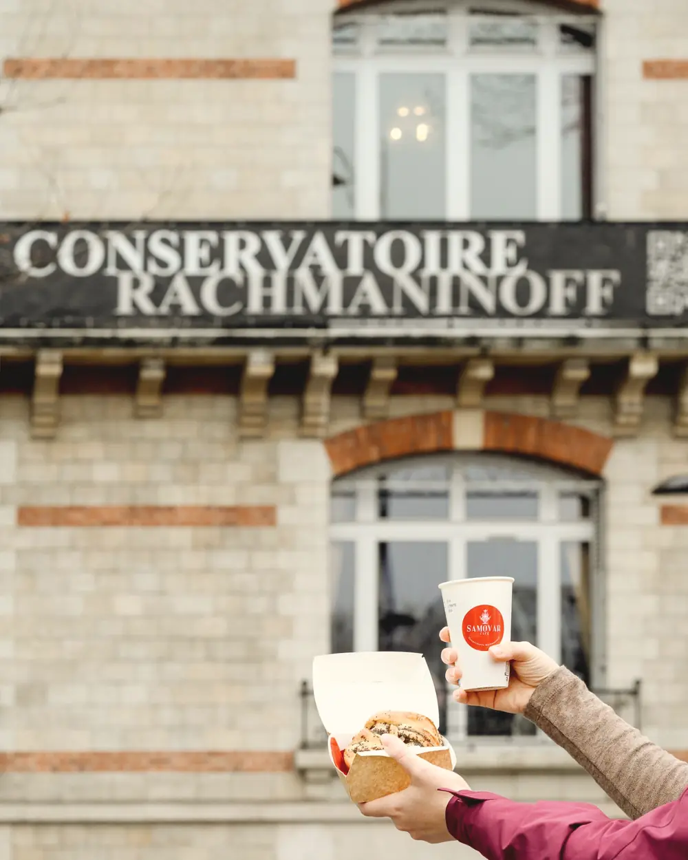 La façade du Conservatoire Serge Rachmaninoff et son enseigne, avec une main qui tend un gobelet du Samovar Café et une barquette.