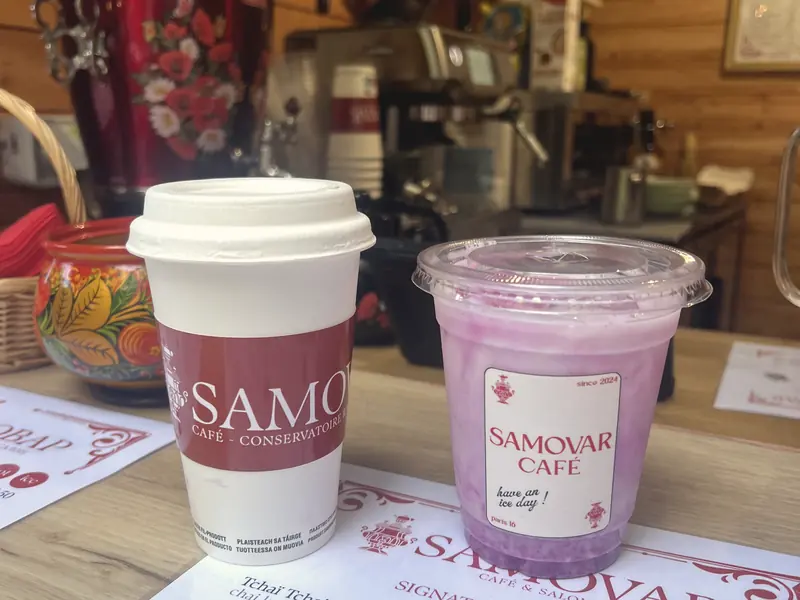Le comptoir en bois avec un samovar rouge peint, un café chaud et une boisson glacée du Samovar Café, posés sur la carte des boissons signature.