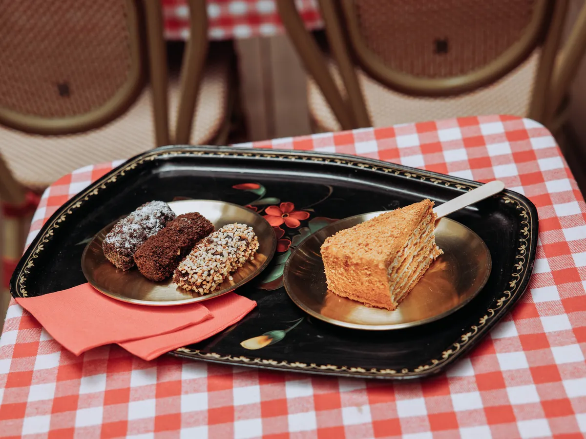 Un plateau peint avec une part de medovik et des gourmandises, sur une table vichy de la terrasse.