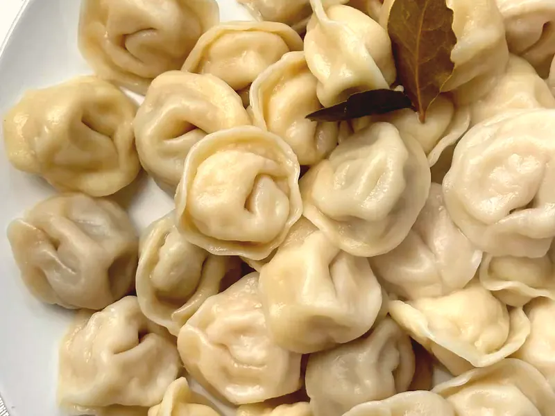 Une assiette de pelmeni tout juste pochés, avec une feuille de laurier.