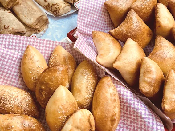 Des pirojki dorés et des blinis roulés, présentés sur une nappe vichy.
