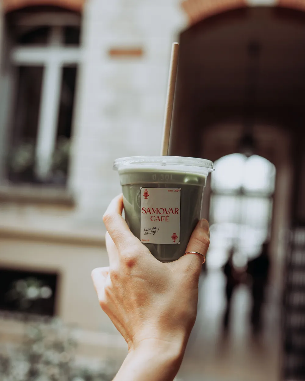 Une main tient un matcha glacé du Samovar Café sous le porche du Conservatoire, qui mène à la cour.