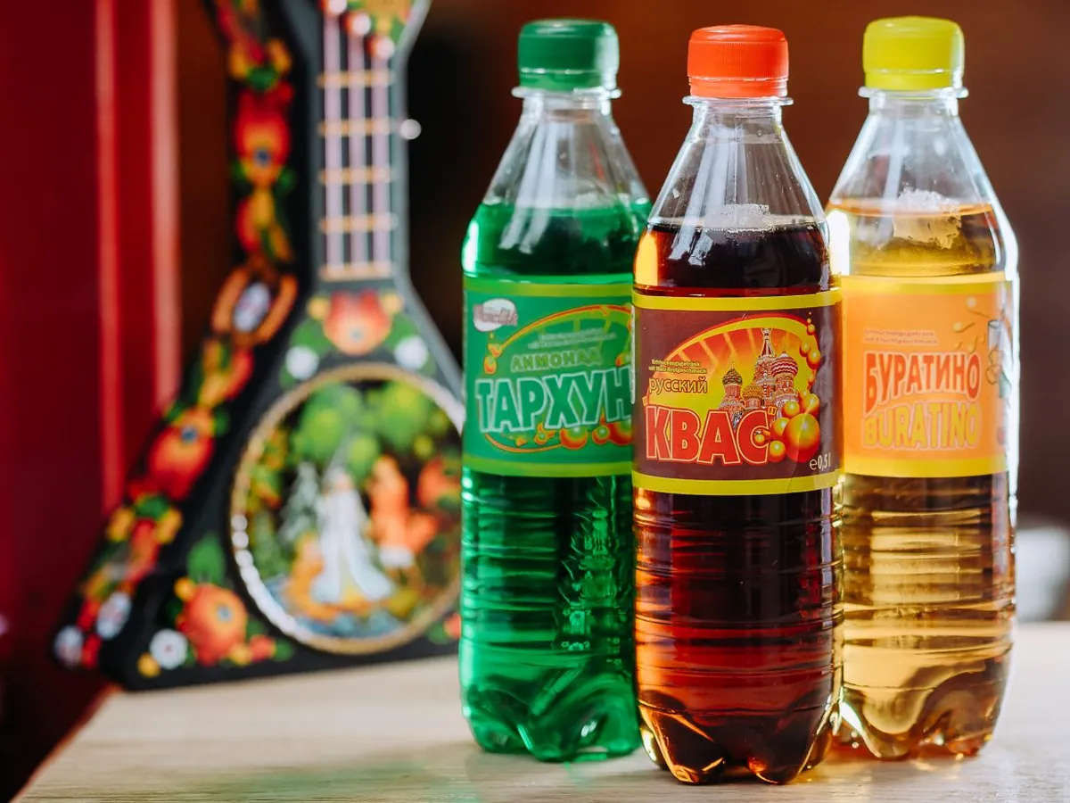Trois bouteilles de sodas de l'Est, tarhun, kvas et Bouratino, devant une balalaïka peinte.