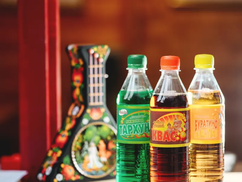 Trois bouteilles de sodas de l'Est, tarhun, kvas et Bouratino, posées près d'une balalaïka peinte.