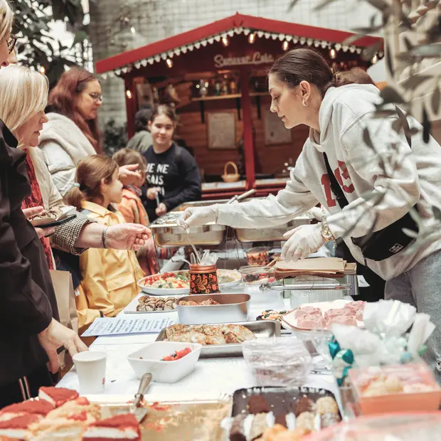 Un buffet dressé dans la cour, servi par une personne de l'équipe devant le kiosque rouge, sous les guirlandes.